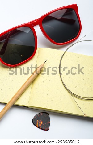 Yellow notepad with pencil, sunglasses, string and mediator on white surface