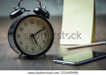 Black vintage alarm clock with notepad and phone