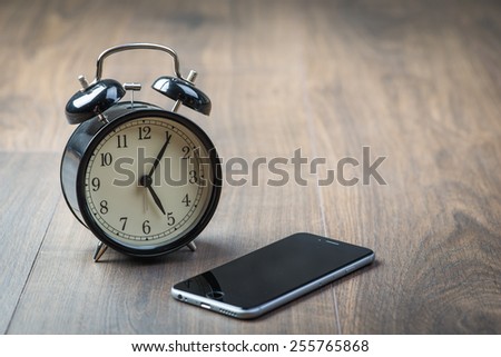 Black vintage alarm clock with phone on a wooden floor