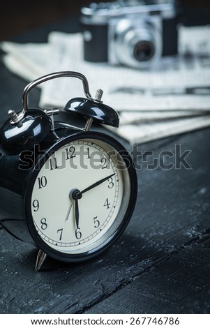 Black alarm clock with camera and newspaper on a wooden table