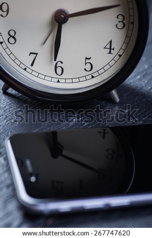 Black alarm clock with cell phone on a wooden table
