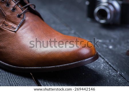 A brown leather shoes with vintage camera on a black wooden floor