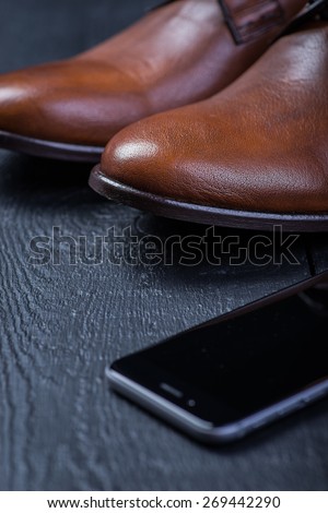 A pair of brown leather shoes with phone on a black wooden floor