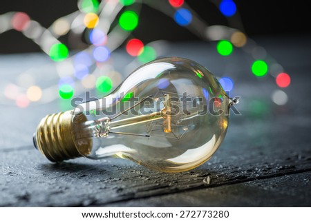Vintage tungsten bulb on a black wooden table with colorful lights at the background