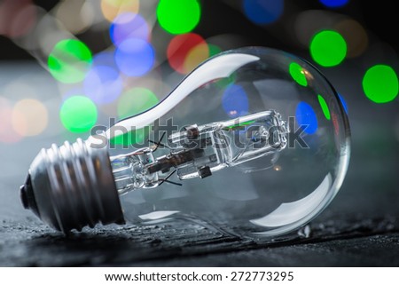 Vintage halogen bulb on a black wooden table with colorful lights at the background