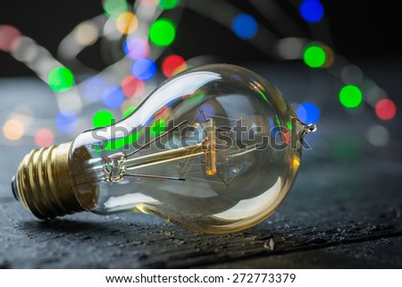 Vintage tungsten bulb on a black wooden table with colorful lights at the background