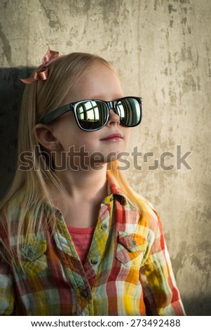 Portrait of a cute little hipster looking girl with sunglasses and bow over the concrete background