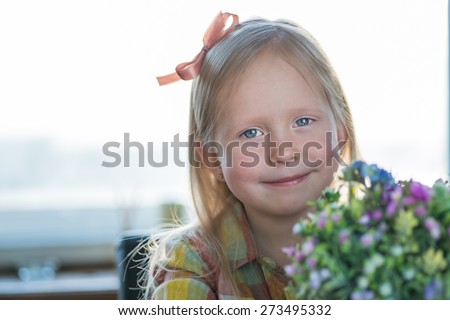 Portrait of a cute little hipster looking girl with flowers and bow over the window background