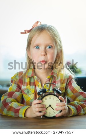 Portrait of a young little hipster looking girl with alarm clock over the window background