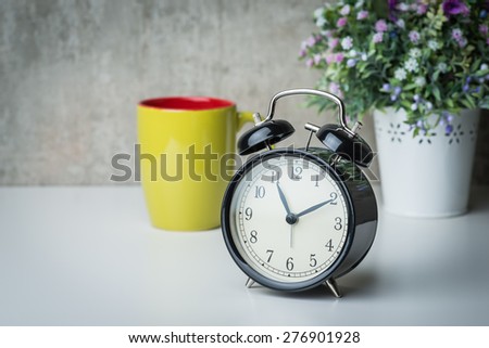 Vintage alarm clock on a night table with flowers and coffee mug