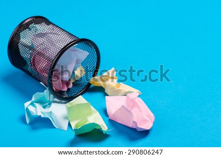 Small black trash bin with crumpled color paper inside over the blue background