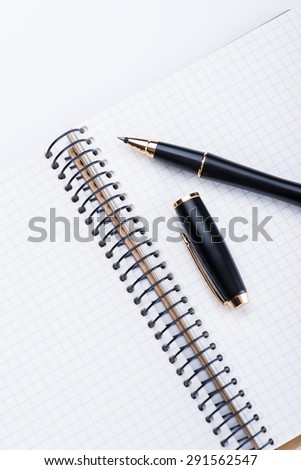 A spiral notebook with black ball pen on the white table, isolated