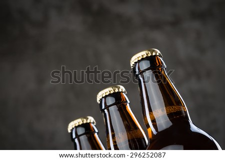 Three ice cold beer bottles in a row over the grey concrete wall background