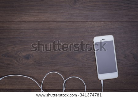 White smart phone with headphones cable on the wooden table