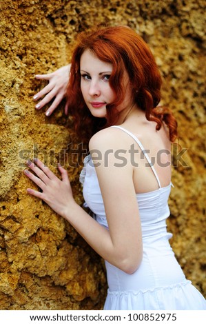 Young redhead sensual woman portrait standing near the rock. Outdoor.
