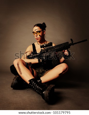 Sexy army woman posing with weapon, on gray background.