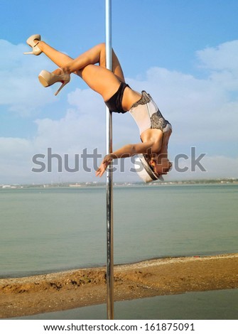 Young slim woman exercise pole dance outdoors.