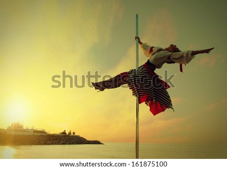 Young sexy woman girl in dress exercise pole dance against sunset sea.