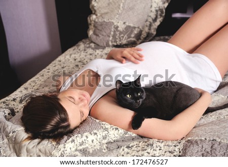 Young smiling pregnant woman with cat at home.