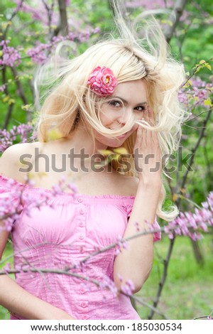 Smiling young woman with blonde long hair in spring park.
