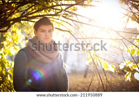 Young guy portrait against an autumn tree in a park, backlighting with bokeh.