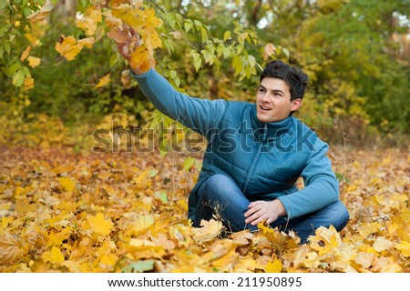 Cool happy guy siiting on autumn foliage in park.