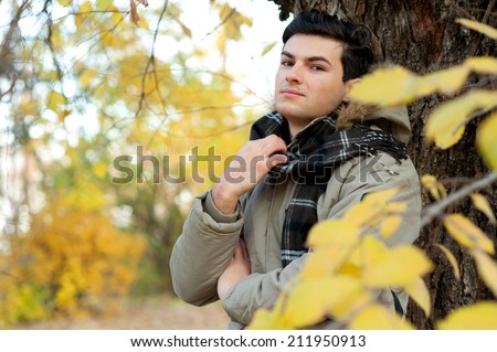Young stylish man portrait dressed in a jacket and plaid scarf relaxing in autumn park.