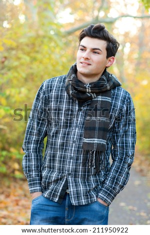 Portrait of the handsome smiling man dressed in a plaid shirt hiking in autumn park.
