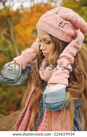 Cute casual woman dressed in pink knitted hat, scarf and gloves posing in autumn park.