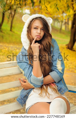 Pretty girl in a knitted bear hat posing in autumn park.