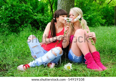 stock photo : two young pretty girls with flowers sitting on a grass