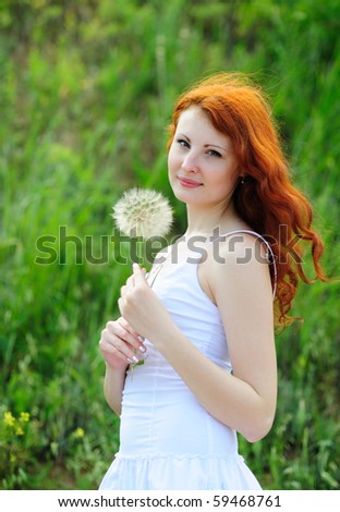 Cute young redhead female with big dandelion in her hands