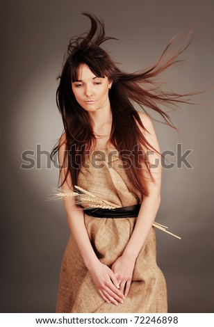 Beautiful young woman with fluttering hair and wheat ears.