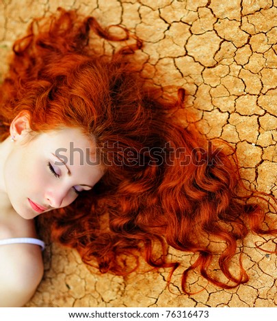 Beautiful young woman with red hair on the dried up ground.