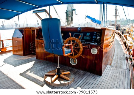 Cockpit inside a boat with a wood wheel and leather chair.