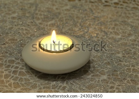 Burning candle in white candlestick holder
