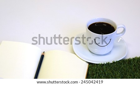 Cup of coffee,note paper,pencil, and grass on office white table.