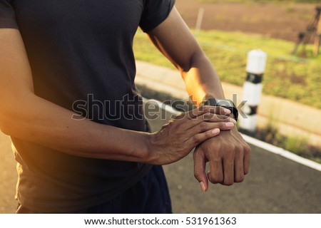 Male runner jogging outside looking at his wearable fitness tracker outside