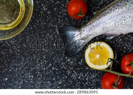 Delicious fresh raw fish on dark granite cutting board with lemon, tomatoes and olive oil. Vintage food background