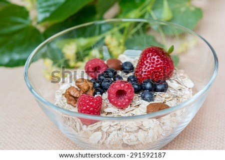 A bowl with hole grain flakes, berries and nuts on sackcloth, beige background. Healthy breakfast