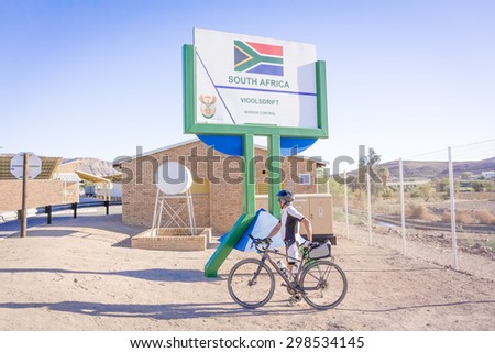 Vioolsdrfif, South Africa - May 3, 2015: Signs at the border between Namibia and Soth Africa. Man on bicycle crossing border.