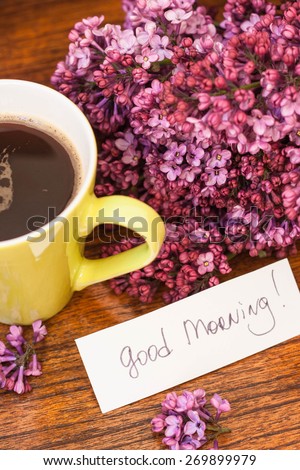 Coffee with lilac and good morning note on the wooden background