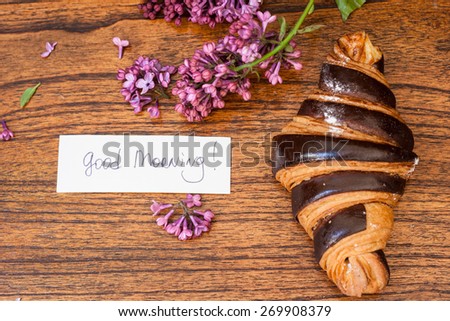 Croissant with good morning note and lilac on the wooden background