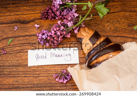 Croissant with good morning note and lilac on the wooden background