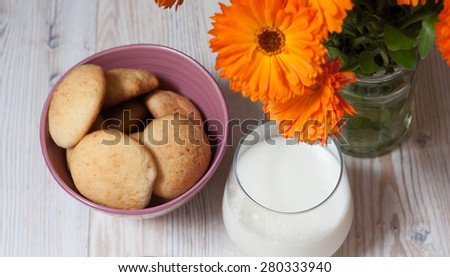 Home made cookies glass of milk and orange flowers in a vase on a white wooden table