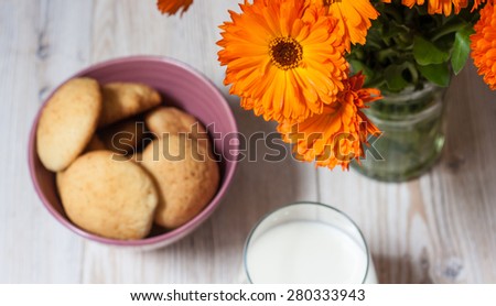 Home made cookies glass of milk and orange flowers in a vase on a white wooden table