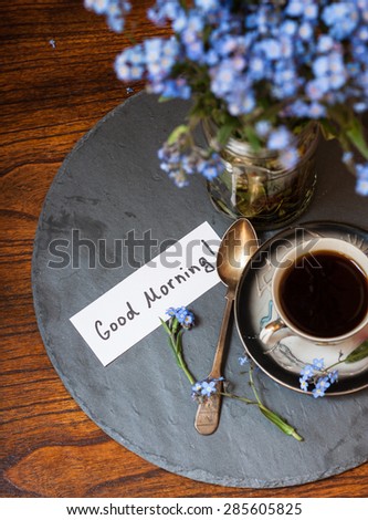 Coffee and blue flowers (forget-me-nots) on a stone and wooden background with good morning note