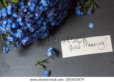 Bunch of blue flowers (forget-me-nots) and good morning note on a black stone background
