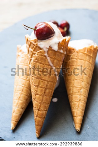 Cherry ice cream in cones with cherry on the top on a dark background