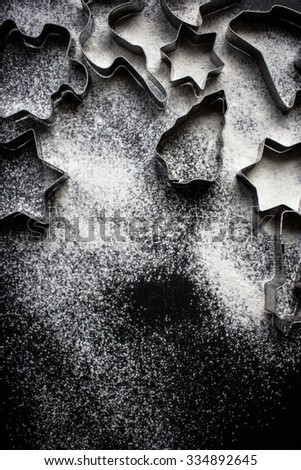 Cookie cutters on a black kitchen background with flour spread all over